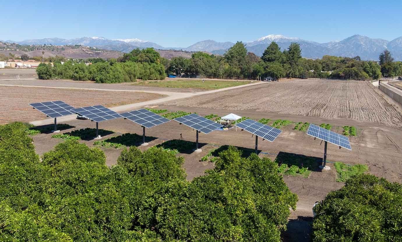 Aerial view of the five-panel agrivoltaic array over crop beds at Spadra Farm, with snow-capped mountains behind