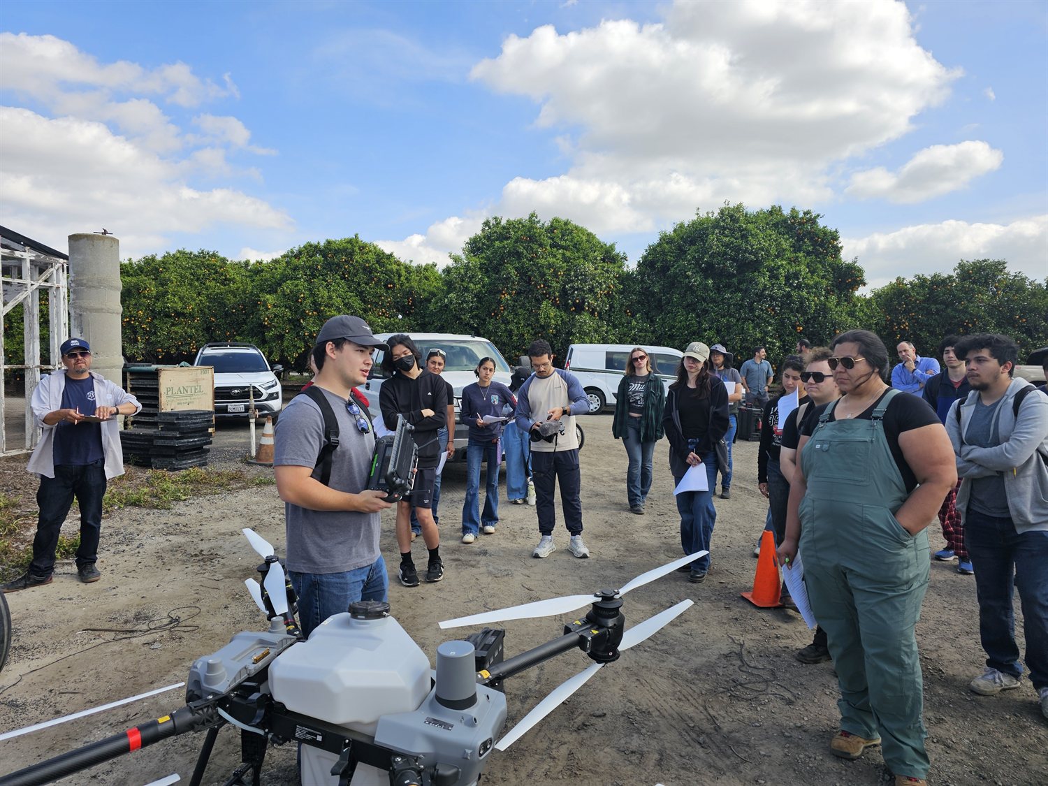 Students gathered around an agricultural spray drone during a precision-agriculture field session in a citrus orchard